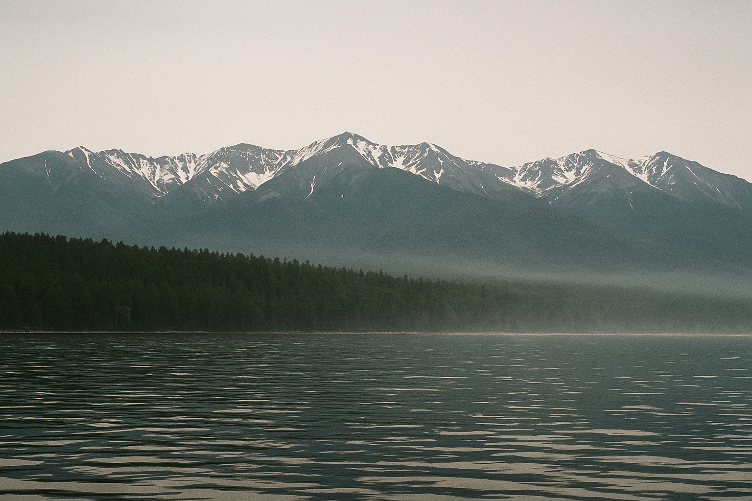Bargusin-Kette mit Schneefeldern über dichter Taiga, die bis ans Ufer reicht, vom Boot aus am Morgen