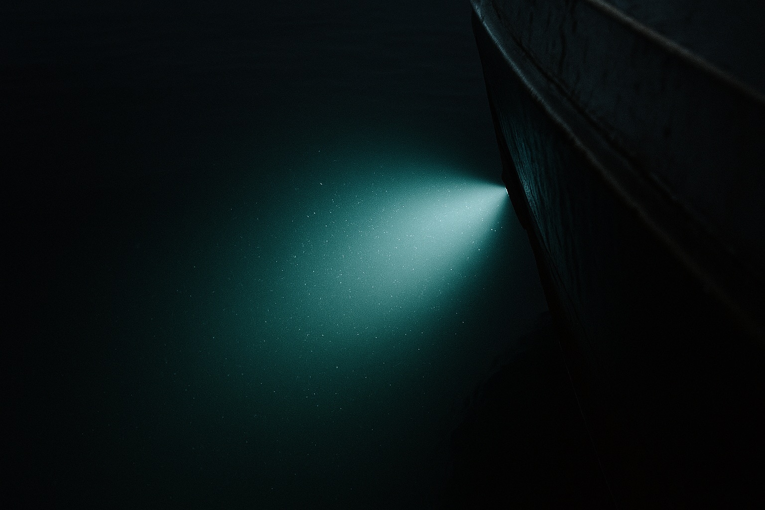 Lichtkegel einer Lampe fällt nachts von einem Schiff in dunkles, tiefes Wasser
