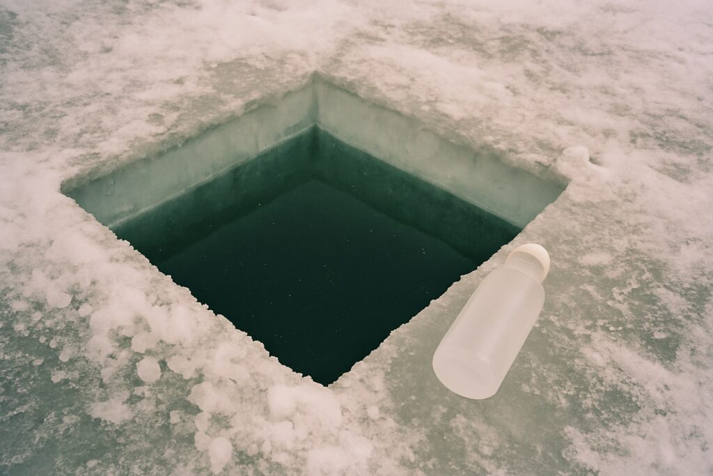 Rechteckiges Probenloch im dicken Klareis mit dunklem Wasser und einer Probenflasche daneben