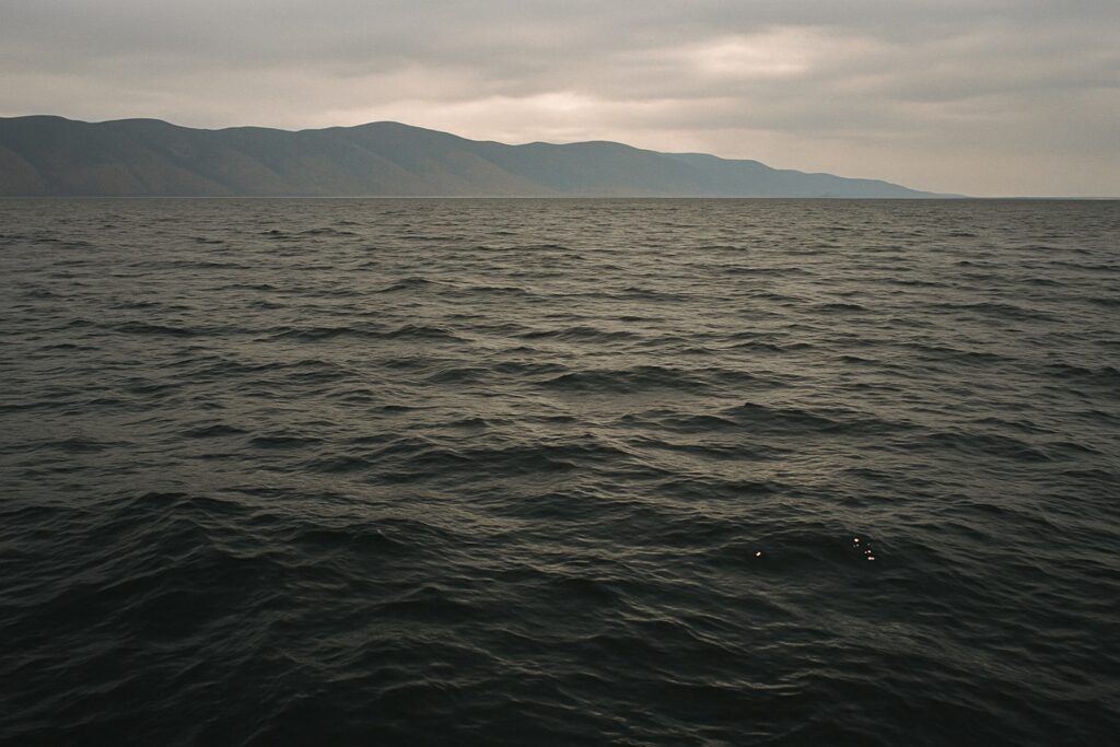 Dunkelblaue Wasserfläche mit leichter Dünung weit draußen auf dem See, am Horizont ein Bergzug